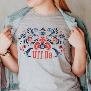 May include: A gray t-shirt with a blue and red floral design and the text "Uff Da" in red.