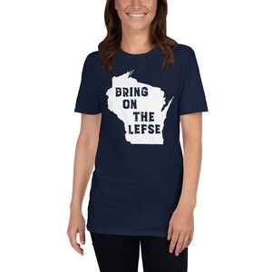 May include: Navy blue t-shirt featuring a white outline of the state of Wisconsin with the text "BRING ON THE LEFSE". The shirt is made of a soft material and has short sleeves.