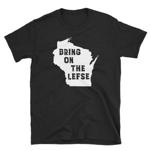 May include: Black t-shirt featuring a white outline of the state of Wisconsin. The text "BRING ON THE LEFSE" is printed in bold, uppercase letters within the state outline. The shirt is made of a soft material.