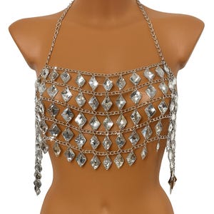 Könnte beinhalten: Silberfarbenes Kettenhemd-Top mit Neckholder-Design. Das Top hat Reihen von rautenförmigen, klaren, funkelnden Verzierungen. Das Kettenhemd fällt über den Oberkörper und erzeugt einen schimmernden Effekt. Ein auffälliges Modeaccessoire.
