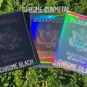 May include: Three passport covers in different colors: chrome black, chrome gunmetal, and chrome silver. Each cover has the words "PASSPORT" and "United States of America" printed on the front.