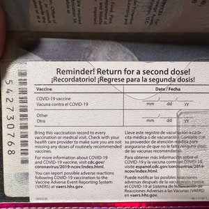 May include: A pink vaccination record card with a barcode and the text "Reminder! Return for a second dose!" and "&iexcl;Recordatorio! &iexcl;Regrese para la segunda dosis!"  The card has spaces to record the date of the vaccine and the type of vaccine.