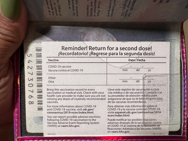 May include: A pink vaccination record card with a barcode and the text "Reminder! Return for a second dose!" and "&iexcl;Recordatorio! &iexcl;Regrese para la segunda dosis!"  The card has spaces to record the date of the vaccine and the type of vaccine.
