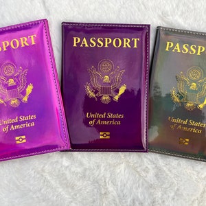 May include: Three passport holders with a holographic finish. The holders are purple, dark purple, and black with a gold shimmer. Each holder has the words "PASSPORT" and "United States of America" printed in gold.