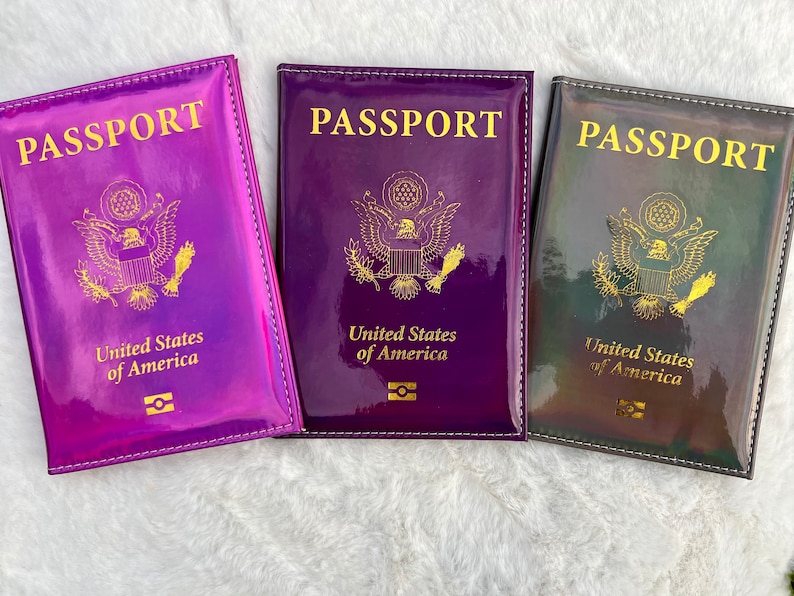 May include: Three passport holders with a holographic finish. The holders are purple, dark purple, and black with a gold shimmer. Each holder has the words "PASSPORT" and "United States of America" printed in gold.