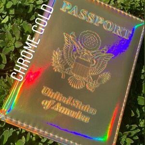 May include: A passport holder with a holographic finish in a chrome gold color. The holder has the words "PASSPORT" and "United States of America" printed on it.