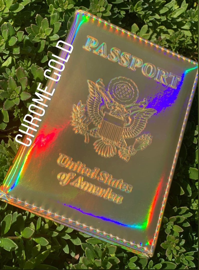 May include: A passport holder with a holographic finish in a chrome gold color. The holder has the words "PASSPORT" and "United States of America" printed on it.