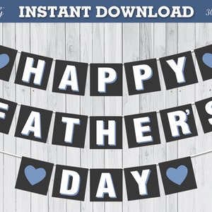 May include: A black and white banner with the text "Happy Father's Day" in white letters with a blue heart on each end. The banner is hanging on a white wood background.