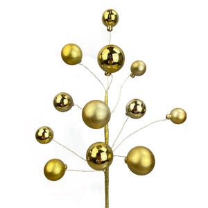 Op de afbeelding: Een decoratieve goudkleurige tak met meerdere gouden bollen van verschillende groottes, bevestigd aan dunne, zilverkleurige draden. De tak heeft een getextureerde, metallic afwerking. De bollen hebben een glanzend, reflecterend oppervlak. De achtergrond is effen wit.