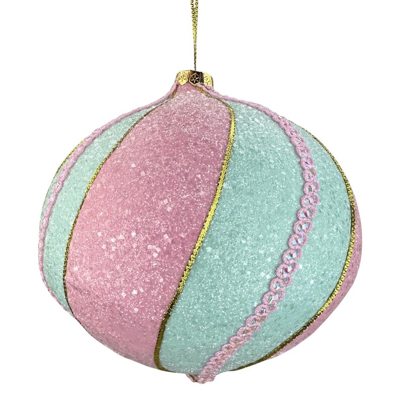 Pu&ograve; includere: Un ornamento natalizio dai colori pastello con una superficie strutturata e glitterata. L'ornamento &egrave; diviso in sezioni rosa e azzurre, separate da finiture dorate. Un bordo in pizzo rosa con piccole perline trasparenti adorna un lato.