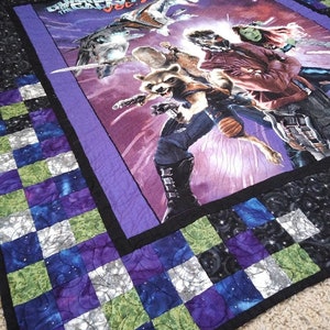 May include: A purple, black, green, and white quilt with a "Guardians of the Galaxy Vol. 2" image in the center. The quilt is made of squares with a galaxy print.