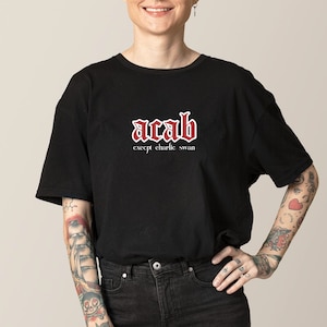 Puede incluir: Camiseta negra con un gráfico rojo "acab" en fuente gótica. El texto "except charlie swan" está impreso en blanco debajo del gráfico.