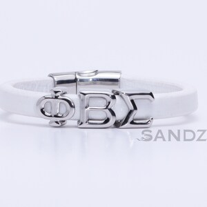 Puede incluir: Pulsera de cuero blanco con un dije plateado que dice "ΦΒΣ".