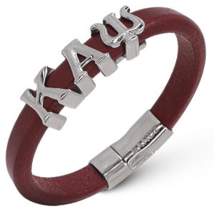 May include: A red leather bracelet with a silver clasp and silver letter charms spelling out "KAUS".