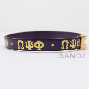 May include: Purple leather bracelet with gold Greek letters "ΩΨΦ" on it.