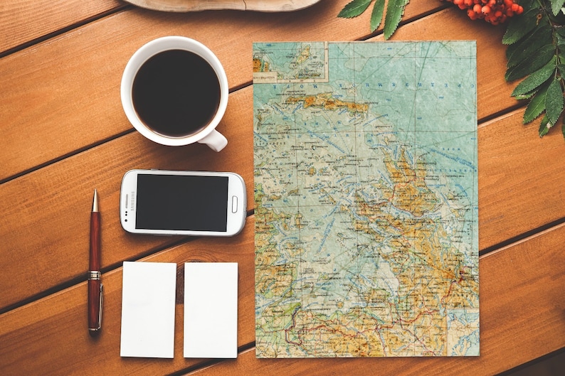 Peut inclure: Une tasse &agrave; caf&eacute; blanche remplie de caf&eacute; noir repose sur une table en bois &agrave; c&ocirc;t&eacute; d'un smartphone blanc, d'un stylo marron, de deux cartes blanches vierges et d'une carte vintage d'une r&eacute;gion c&ocirc;ti&egrave;re.