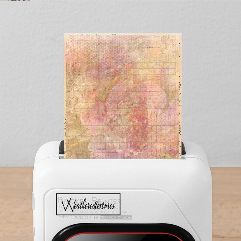 Op de afbeelding: Een witte printer met een rode accent aan de onderkant. De printer heeft een label met de tekst "Rocket Printer by Weatheredtextures High Resolution Print Head 1200x1200dpi Memobird G4 2hrs Fast Charge". Een vel papier met een bloemenontwerp wordt in de printer gevoerd.