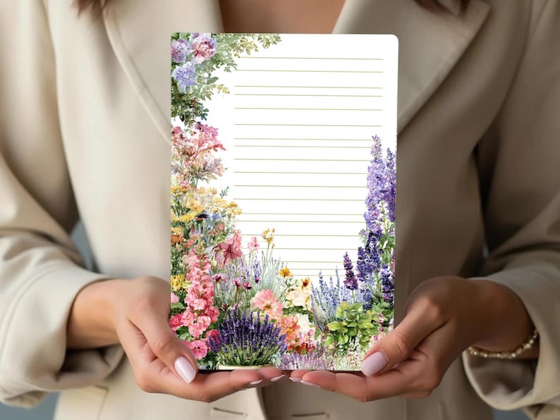 May include: A lined notepad with a floral border featuring pink, purple, yellow, and green flowers. The notepad is held by a person wearing a beige blazer.