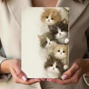 May include: A rectangular print featuring six fluffy kittens with various fur colors, including brown, gray, and cream. The kittens peek out from behind a white surface, creating a charming and whimsical scene. The print is held by a person.