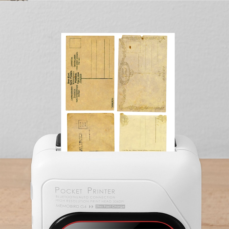 May include: A white pocket printer with the text "POCKET PRINTER", "BLUETOOTH/AUTO CONNECTION", "HIGH RESOLUTION PRINT HEAD 3060", "MEMOBIRD G4", and "2hrs Fast Charge" printed on the front. The printer is loading a stack of vintage postcards.