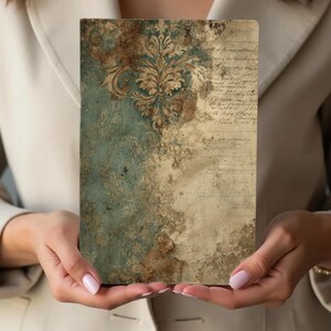 May include: A rectangular, vintage-style journal with a distressed teal and beige design. The top half features a gold floral pattern, while the bottom half has aged script. The journal is held in front of a neutral background.