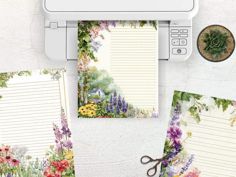 May include: Stationery set with floral designs. The set includes lined paper with a watercolor illustration of a cottage and garden, and additional sheets with floral borders. A printer and a succulent plant are also visible.