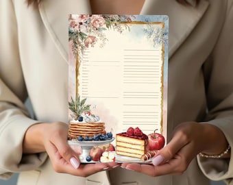 Puede incluir: Un bloc de notas de recetas estilo acuarela con un borde floral e ilustraciones de panqueques, pastel y fruta. El bloc de notas tiene páginas rayadas para escribir recetas. El diseño presenta una estética vintage con colores suaves y un borde decorativo.
