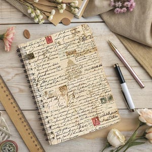 Pu&ograve; includere: Un taccuino a spirale con un design di lettere vintage, con francobolli e scritte a mano. Un righello di legno, penne e fiori sono disposti attorno al taccuino su una superficie di legno chiaro. La copertina del taccuino ha uno sfondo color crema.