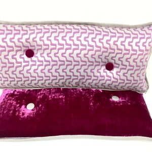 May include: Two decorative throw pillows with button accents. The top pillow has a white background with a pink wavy pattern. The bottom pillow is a solid dark pink.