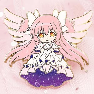 May include: A pink enamel pin featuring an anime-style character with pink hair, angel wings, and a white dress with a purple skirt. The pin has gold-colored metal accents and is set against a pink background.