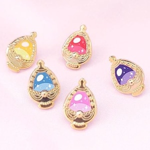 May include: Five gold-colored enamel pins shaped like teardrops with different colored gems inside. The gems are yellow, red, blue, pink, and purple.