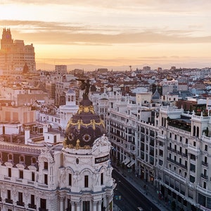 May include: A white building with a gold dome and the word "METROPOL" on the side. The building is surrounded by other buildings and a street with cars and people.