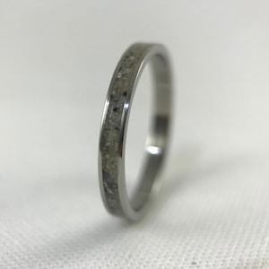 Pode incluir: Um anel de prata com uma banda fina de material cinza embutido.