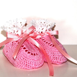 May include: A pair of pink crocheted baby booties with white lace trim and a pink satin ribbon tied around them.