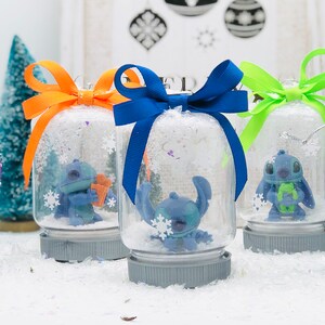May include: Five snow globes with blue Stitch characters inside. Each globe has a different colored bow on top. The globes are sitting on a white surface.