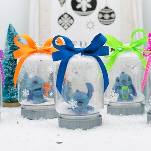 May include: Five snow globes with blue Stitch characters inside. Each globe has a different colored ribbon tied around the top. The globes are sitting on a white surface.