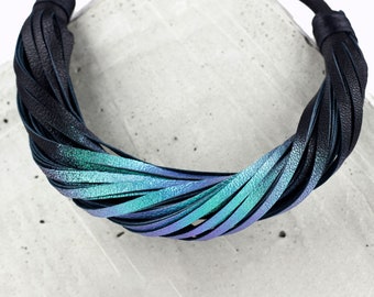 May include: A black leather necklace with a gradient of blue and green colors. The necklace is made of multiple strands of leather that are woven together.
