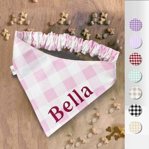 May include: Pink and white gingham dog bandana with the name "Bella" embroidered in burgundy. The bandana has a gathered pink elastic band and is surrounded by dog treats. A color chart with different gingham patterns is on the right.