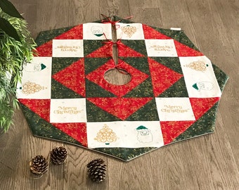 May include: A hexagonal fabric Christmas tree skirt featuring a patchwork design of red, dark green, and white squares. The white squares display gold-colored Christmas trees, Santa Claus faces, and the text Merry Christmas in gold script.