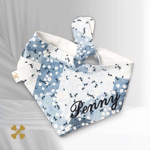 May include: A blue and white bandana with a floral pattern and the name "Penny" embroidered on it. The bandana has a tie-on closure.