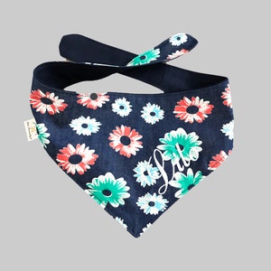 May include: A navy blue bandana with a white floral pattern and the word "Lula" written in white script. The bandana has a red, white, and green floral pattern.