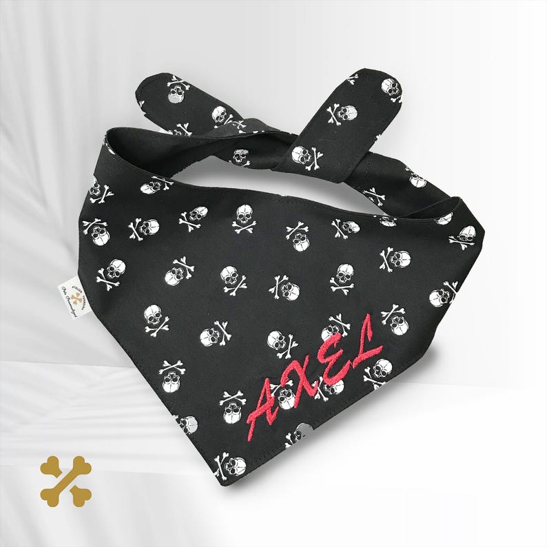 May include: Black bandana with a white skull and crossbones pattern. The bandana has the name "AXEL" embroidered in red.