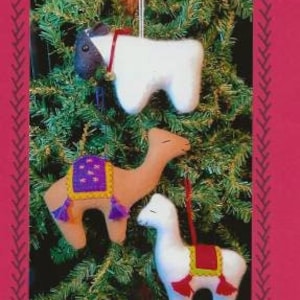 May include: A set of three felt ornaments: a white sheep, a brown camel with a purple and gold saddle, and a white alpaca with a red and gold saddle. The ornaments are hanging on a green Christmas tree.