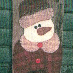 May include: A felt snowman wall hanging with a red hat, white face, and brown eyes. The snowman is wearing a brown coat with a white collar and three red buttons. The snowman is holding a bouquet of red flowers.