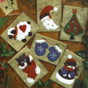 Peut inclure: Ensemble de huit sacs cadeaux de Noël en feutre avec différents thèmes de vacances. Les sacs sont beiges avec un bord cousu et présentent des appliqués d'un mouton, du Père Noël, d'un sapin de Noël, de mitaines, d'un chat dans une chaussette et d'un bonhomme de neige. Les sacs ont une vue arrière montrant un motif floral rouge et blanc.