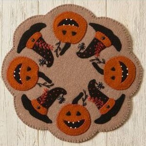 May include: A brown felt circle with five orange pumpkins and five black witch hats with red polka dots. The pumpkins have black eyes, noses, and mouths. The hats have a black brim and a pointed top. The circle is decorated with black spiders and green leaves.