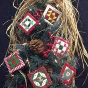 May include: A collection of seven handmade quilted ornaments in various Christmas patterns, including red and white, green and white, and red and yellow. The ornaments are hanging on a small artificial Christmas tree.