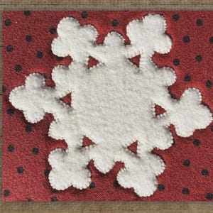 May include: A white felt snowflake applique on a red background with black polka dots. The snowflake is stitched onto the red felt. The image is a close-up of a holiday decoration.