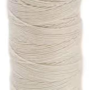 May include: A spool of off-white Sulky Cotton Petites Art thread. The label at the top reads "Sulky 712-1082" with a barcode and other text. The bottom label reads "Staple Cotton". The thread is tightly wound on the spool.