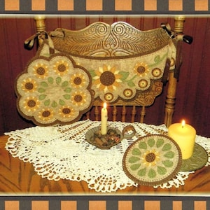 May include: Two brown and green quilted sunflower pot holders with a crocheted doily and two lit candles on a wooden table.